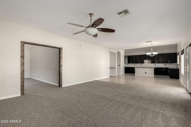 unfurnished living room featuring ceiling fan with notable chandelier, a sink, visible vents, baseboards, and dark carpet