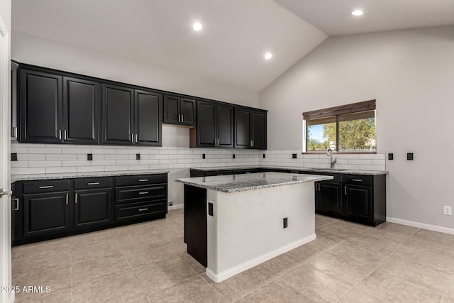 kitchen featuring backsplash, a kitchen island, a sink, light stone countertops, and dark cabinets