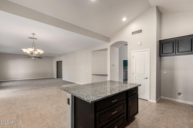 kitchen with arched walkways, visible vents, open floor plan, a kitchen island, and light stone countertops