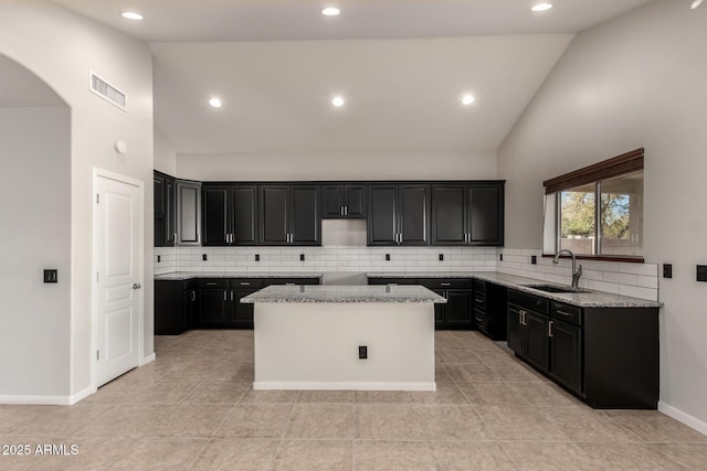 kitchen featuring visible vents, a kitchen island, a sink, light stone countertops, and dark cabinets