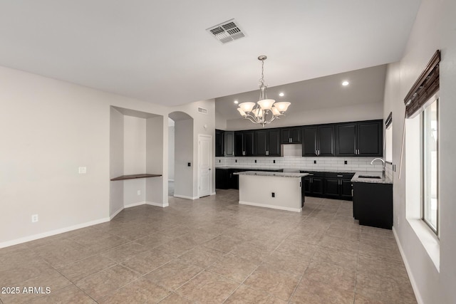 kitchen featuring visible vents, arched walkways, decorative backsplash, a center island, and dark cabinetry