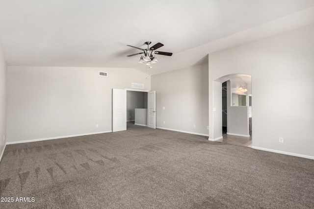 unfurnished bedroom with arched walkways, dark colored carpet, vaulted ceiling, and visible vents