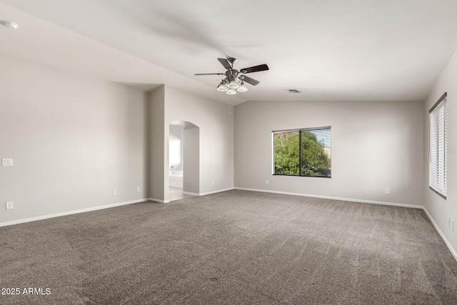 empty room featuring arched walkways, lofted ceiling, visible vents, carpet flooring, and baseboards