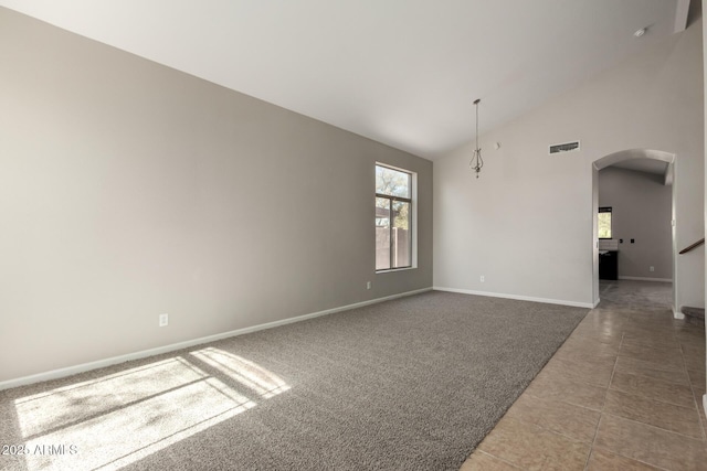 carpeted empty room featuring arched walkways, visible vents, high vaulted ceiling, baseboards, and tile patterned floors