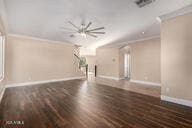 unfurnished living room with baseboards, wood finished floors, visible vents, and crown molding