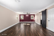 unfurnished living room featuring ornamental molding, a barn door, wood finished floors, and baseboards