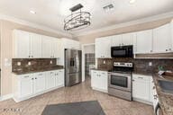 kitchen with hanging light fixtures, ornamental molding, stainless steel appliances, and white cabinets