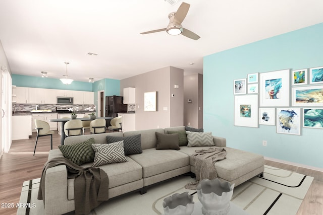 living room with ceiling fan, sink, and light wood-type flooring