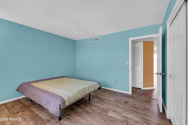 bedroom with baseboards, visible vents, and wood finished floors