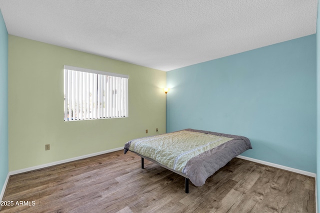 bedroom with a textured ceiling, baseboards, and wood finished floors