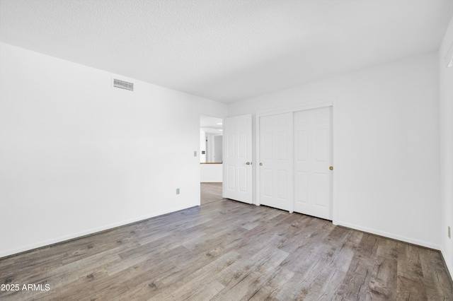 unfurnished bedroom featuring a closet, visible vents, a textured ceiling, wood finished floors, and baseboards