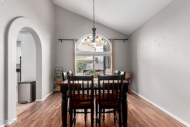 dining room featuring vaulted ceiling, wood finished floors, arched walkways, and a chandelier