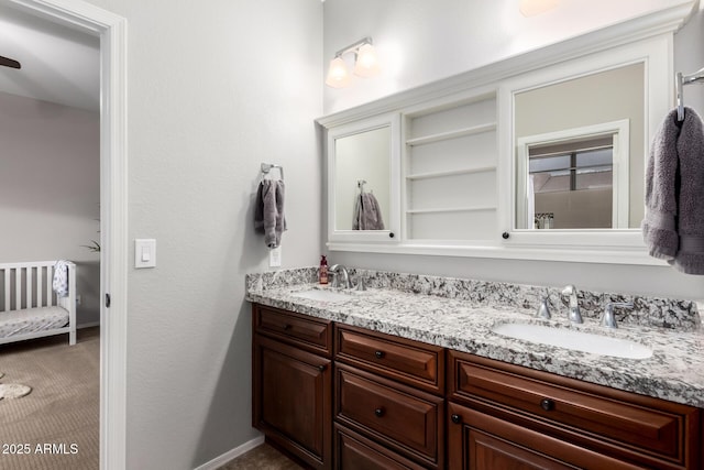 ensuite bathroom featuring double vanity, connected bathroom, baseboards, and a sink