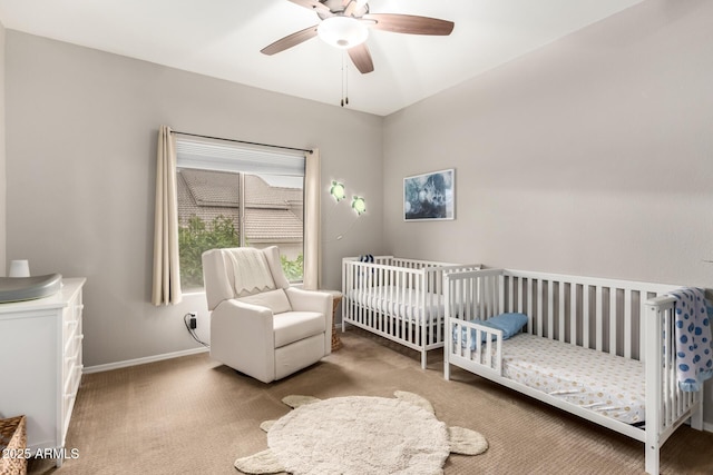 bedroom featuring a nursery area, ceiling fan, baseboards, and carpet floors