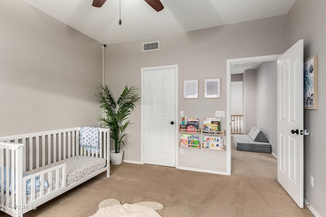 carpeted bedroom featuring visible vents, a crib, baseboards, and a ceiling fan