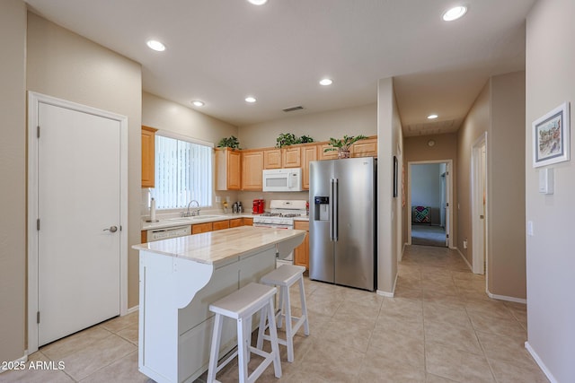 kitchen with sink, a center island, light tile patterned floors, light brown cabinets, and white appliances