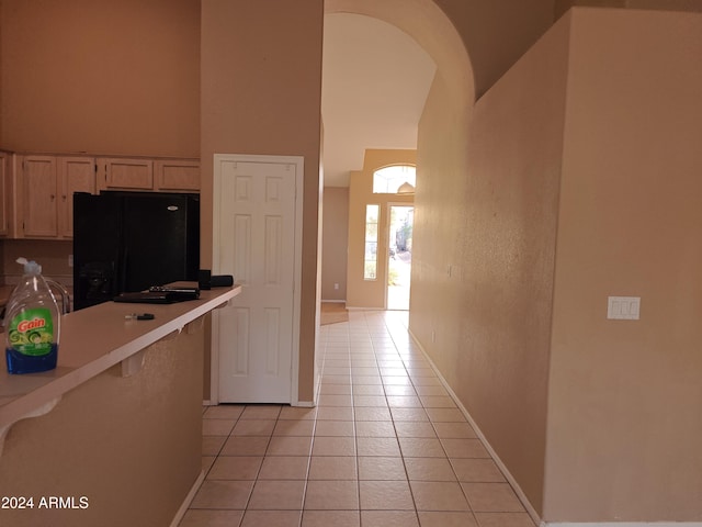 kitchen featuring light brown cabinets, black fridge, a towering ceiling, and light tile patterned floors