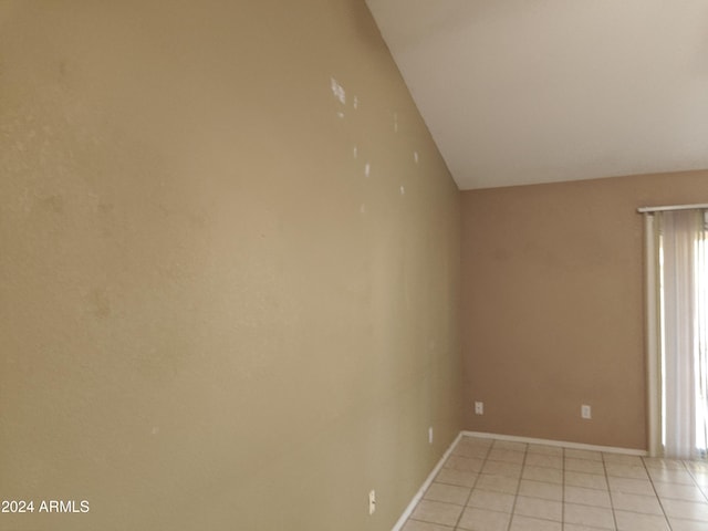 tiled spare room featuring lofted ceiling