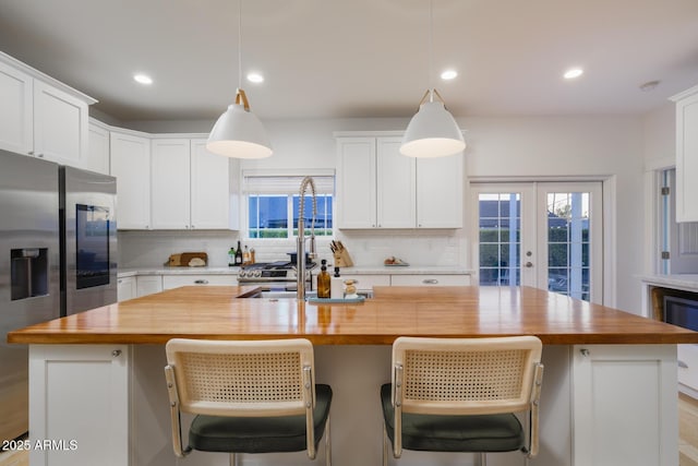 kitchen featuring white cabinetry, a kitchen island with sink, butcher block countertops, and decorative light fixtures