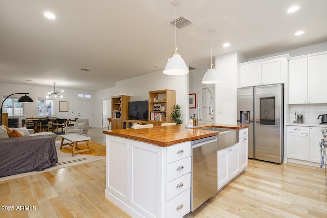 kitchen featuring stainless steel appliances, butcher block counters, white cabinets, and decorative light fixtures