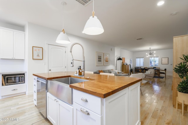 kitchen featuring pendant lighting, appliances with stainless steel finishes, an island with sink, and white cabinets