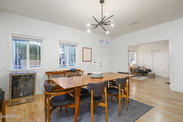 dining area with light wood-type flooring, heating unit, beverage cooler, and a chandelier