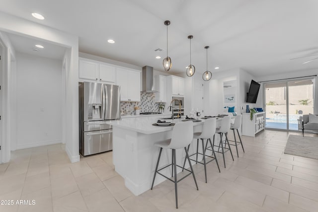 kitchen with wall chimney exhaust hood, white cabinetry, stainless steel fridge with ice dispenser, and an island with sink