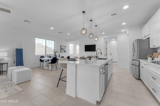 kitchen with a breakfast bar, white cabinets, sink, hanging light fixtures, and an island with sink