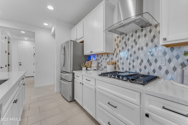 kitchen featuring white cabinets, stainless steel appliances, light stone counters, and wall chimney exhaust hood