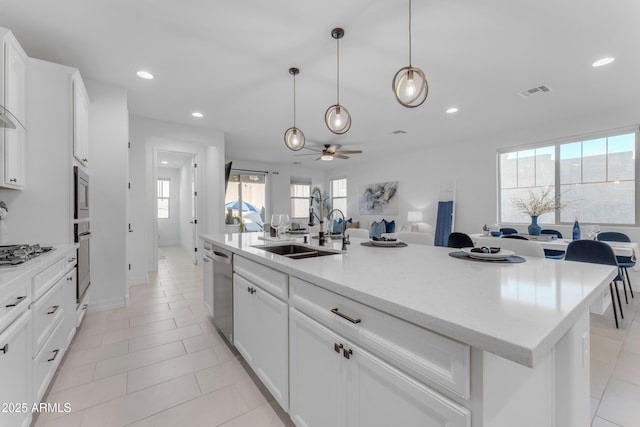 kitchen with a center island with sink, sink, decorative light fixtures, light tile patterned flooring, and white cabinetry