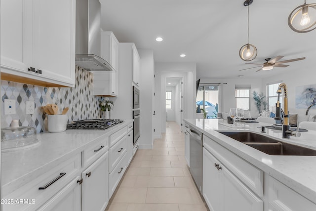 kitchen with white cabinets, sink, wall chimney exhaust hood, appliances with stainless steel finishes, and light stone counters