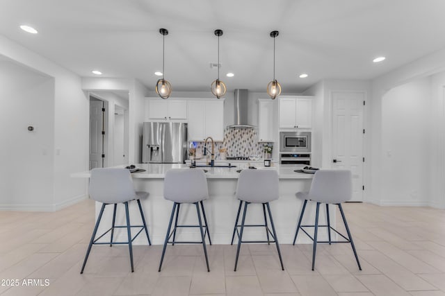 kitchen featuring decorative light fixtures, wall chimney exhaust hood, appliances with stainless steel finishes, a large island, and a kitchen bar