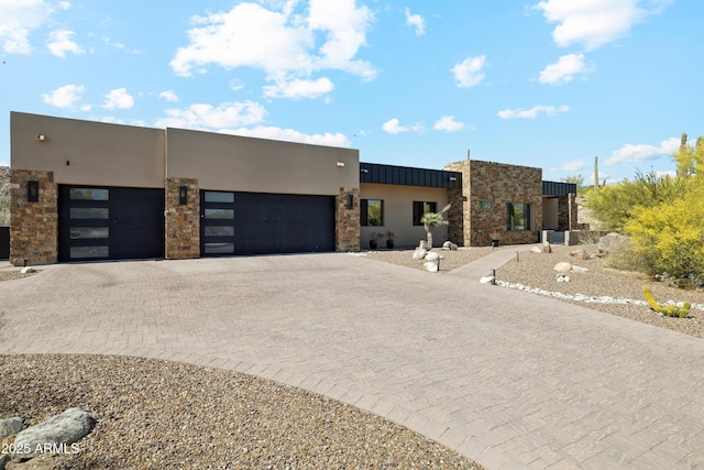 modern home featuring an attached garage, stucco siding, decorative driveway, and stone siding