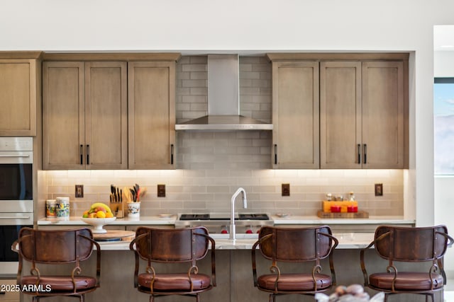 kitchen featuring a kitchen breakfast bar, stainless steel double oven, wall chimney exhaust hood, and tasteful backsplash