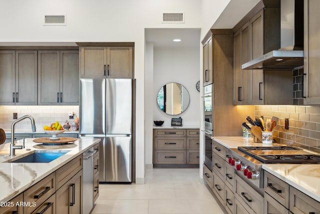 kitchen with visible vents, light stone countertops, a sink, stainless steel appliances, and wall chimney exhaust hood