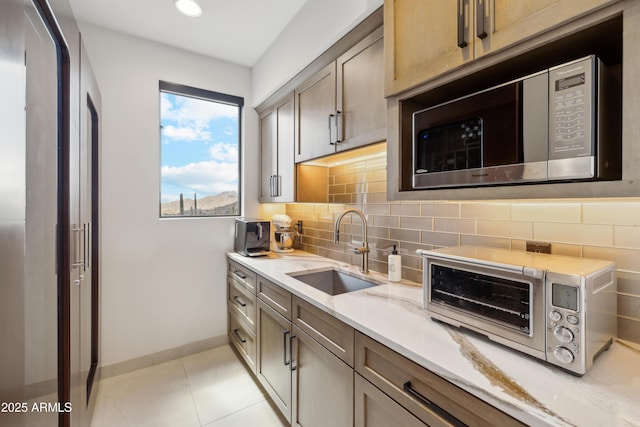 kitchen with a sink, baseboards, stainless steel microwave, decorative backsplash, and a toaster
