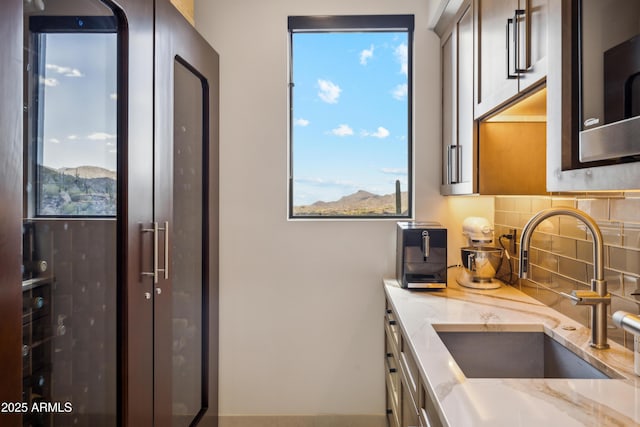 kitchen with a sink, light stone counters, decorative backsplash, and stainless steel microwave