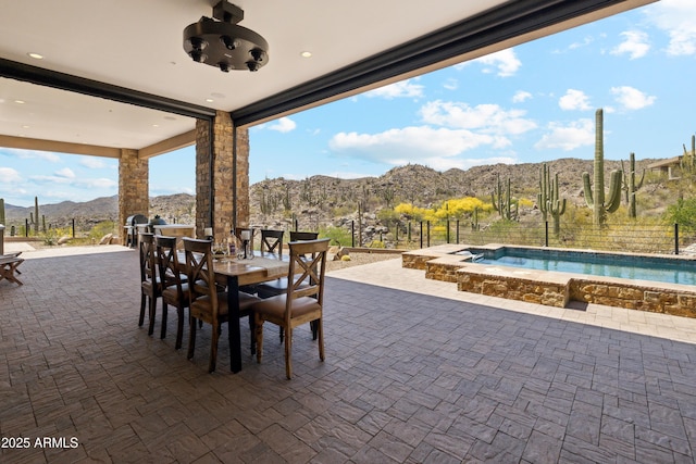 view of patio featuring a jacuzzi, fence, outdoor dining area, and a mountain view