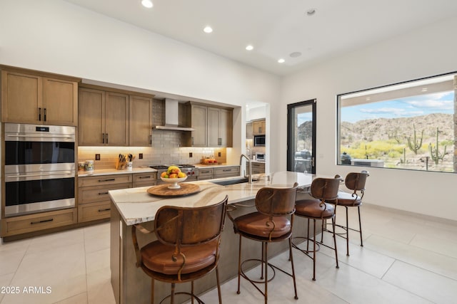 kitchen with wall chimney range hood, appliances with stainless steel finishes, a sink, a kitchen breakfast bar, and tasteful backsplash
