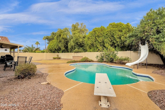 view of swimming pool featuring a fenced in pool, a patio, a water slide, a fenced backyard, and a diving board