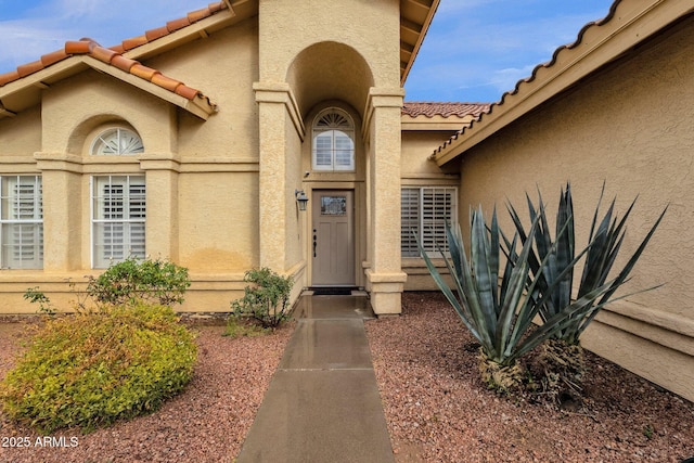 view of exterior entry with a tiled roof and stucco siding