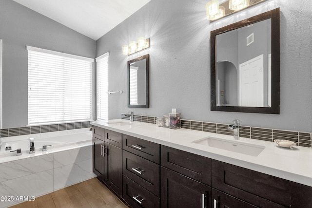 bathroom with lofted ceiling, wood finished floors, a sink, and a bath