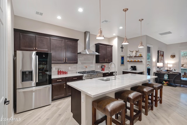 kitchen featuring wall chimney range hood, hanging light fixtures, appliances with stainless steel finishes, light hardwood / wood-style floors, and a breakfast bar area