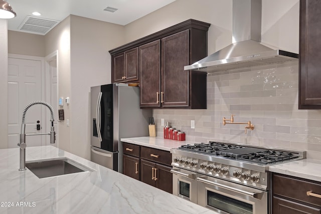 kitchen with light stone countertops, sink, wall chimney exhaust hood, stainless steel appliances, and backsplash