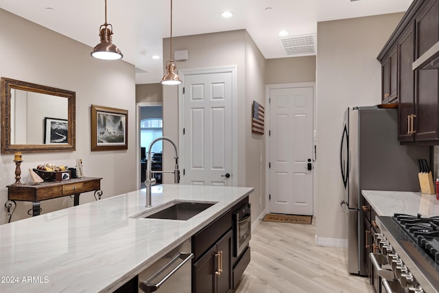 kitchen featuring light stone countertops, dark brown cabinetry, sink, light hardwood / wood-style floors, and hanging light fixtures