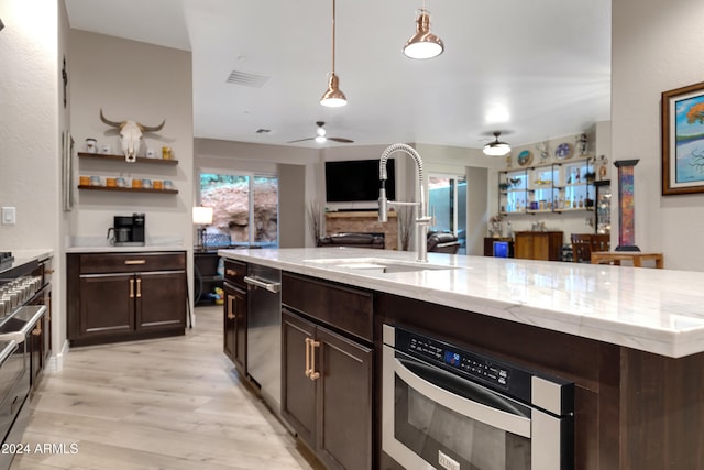 kitchen featuring a center island with sink, sink, hanging light fixtures, light hardwood / wood-style flooring, and dark brown cabinetry