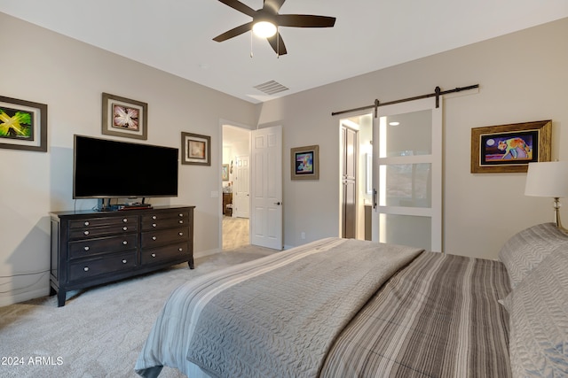 carpeted bedroom with a barn door, ensuite bathroom, and ceiling fan