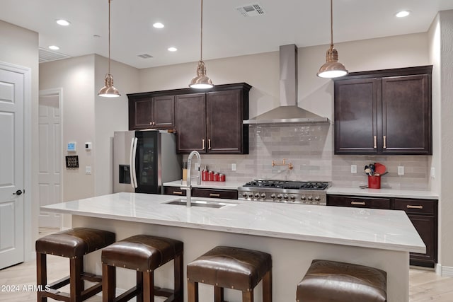 kitchen featuring sink, wall chimney exhaust hood, stainless steel appliances, and a center island with sink