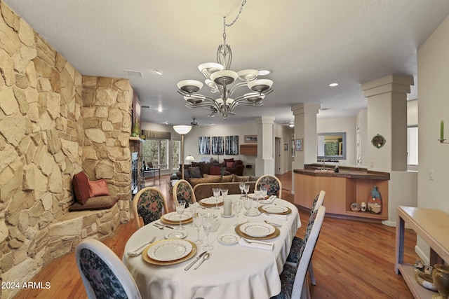 dining space with ornate columns, a stone fireplace, hardwood / wood-style floors, and a chandelier