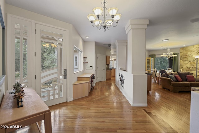 entryway featuring an inviting chandelier, ornate columns, a healthy amount of sunlight, and light wood-type flooring